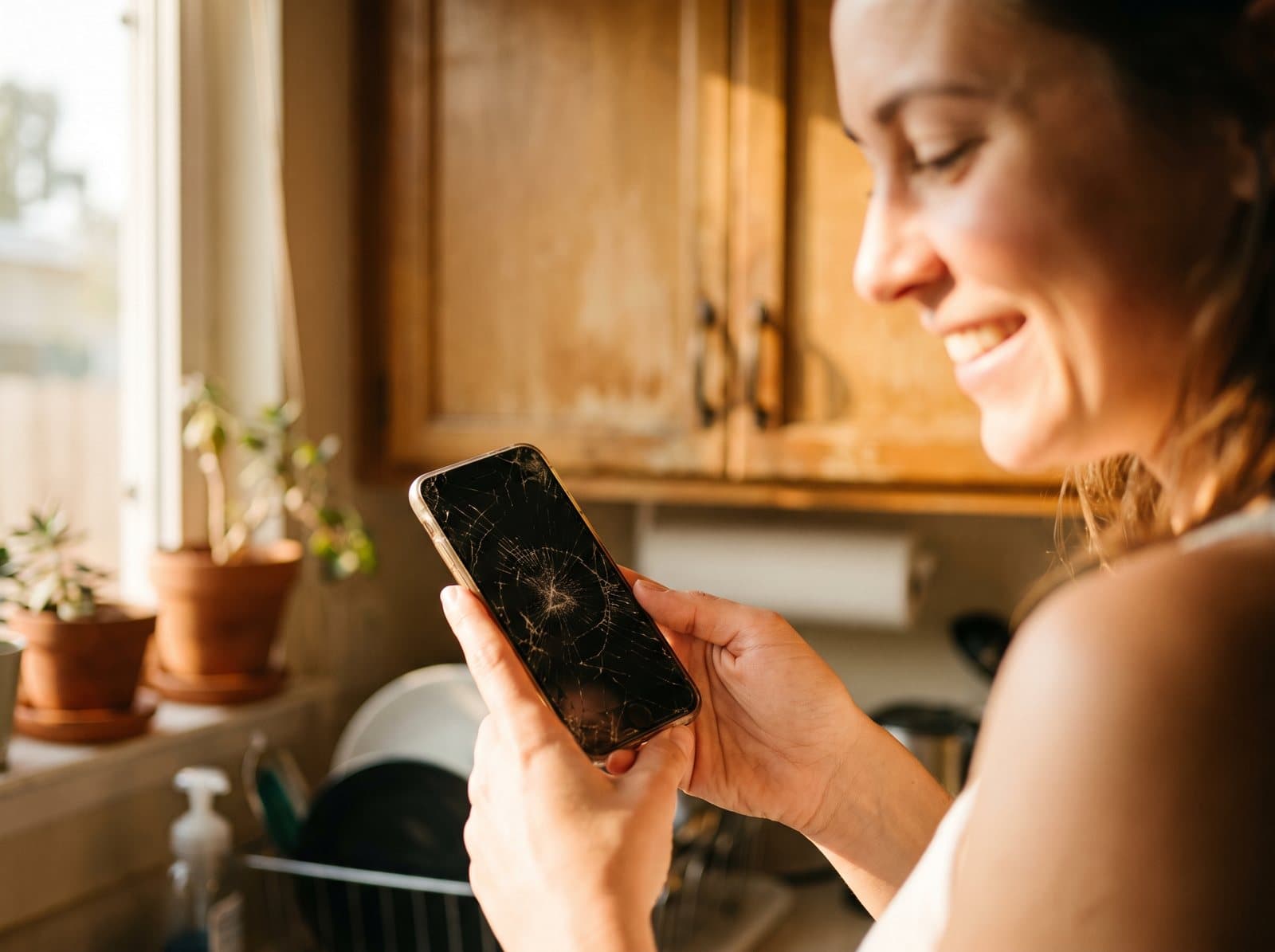A woman looking at the cracked screen of her phone at home